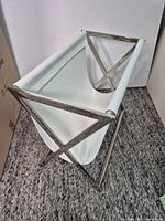 Angled view showing white leatherette sling and stainless steel X-frame