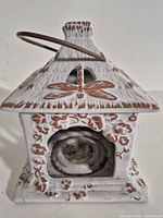 Front view of square white glazed terra cotta lantern showing dragonfly cut-out, leaf relief, votive cavity