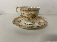 Side view of teacup on saucer showing floral pattern and gold detailing