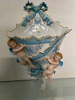 Full view of porcelain wall pocket showing overall design, blue bow, scalloped rim and cherubs