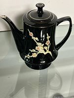 full view right side of black teapot with blossom design and lid