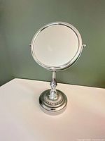 Front view of chrome tabletop vanity mirror showing reflective surface and pedestal base
