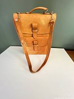 Front view of tan leather satchel showing flap, buckle straps, shoulder strap and top handle
