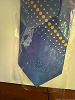 Tie blade with crest and polka dot pattern visible through plastic