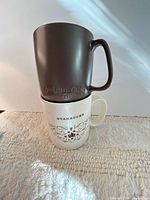 Brown ceramic mug stacked on white bone-china mug