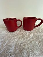 Two red Tim Hortons mugs side by side on fabric surface