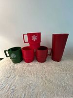 Front view of all five pieces: four stacking mugs (three red, one green) and tall red pitcher