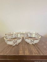 Group view of five matching clear glass bowls showing frosted motifs and gold rims
