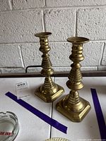 Front view of both brass candlestick holders showing overall design and patina