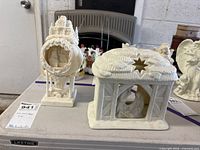 Round village scene luminary shell and rectangular stable luminary side by side
