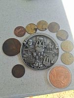 Group shot of all ten coins laid out; central McDonald’s medallion, Hoover Dam coin in capsule, D.A.R.E. token, Marines token, First Coining Meeting token and five angel tokens