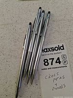 Five silver-tone Cross writing instruments on counter with lot tag