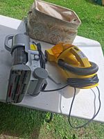 Eureka handheld vacuum, Shark stick vacuum, patterned fabric bag, cords visible on table