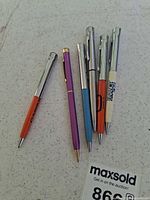 Six Garland pens laid out on table showing barrels, clips and advertising