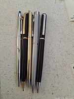 Five metal Quill pens laid out showing finishes and size