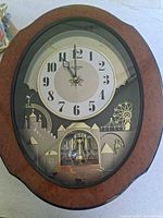 Front view of Rhythm Small World musical wall clock showing full frame, dial, and pendulum window