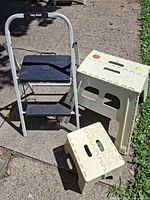 Group shot of one metal two-step ladder and two beige plastic folding stools