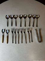 Full set of spoons, forks, and tongs laid out on tabletop
