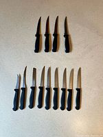 Top row of 4 serrated knives, bottom row of 10 straight knives displayed on countertop