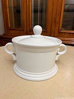 Front view of white ceramic crock with lid and handles