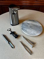 All items grouped: can opener, marble Lazy Susan, corkscrew, peeler, two ice tongs