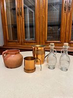 Group shot of all five items: two copper jugs, terracotta pot, two glass cruets