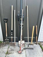 Group of seven long-handled garden tools leaning against doors