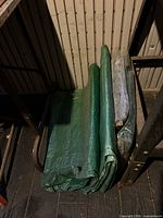 Stack of four folded tarps: three green, one light grey in sleeve