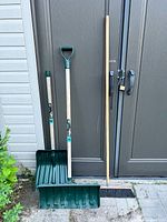 Three long-handled tools: two green snow shovels and one push broom