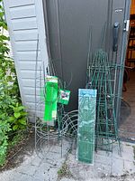 Lot overview leaning against shed: trellises, tomato cages, rings, unopened stakes