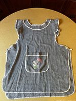 Blue gingham smock apron laid flat showing pocket and side buttons
