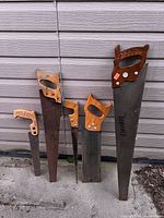 Group of five vintage hand saws leaning against siding
