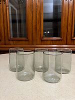 Five smoky grey cylindrical glass tumblers on counter
