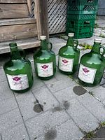 Four green glass wine jugs with labels shown outdoors