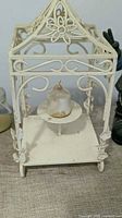 Front view of white metal scrollwork candle holder with votive