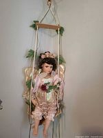 Porcelain fairy doll seated on wooden swing with ivy decoration