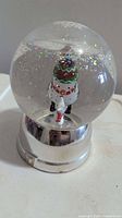 Front view of glass snow globe with snowman and dog on silver base