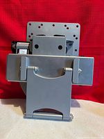 Front view of grey metal TV wall mount bracket showing VESA plate, hinge, and mounting hardware