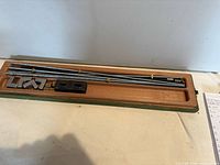 Open wooden case showing steel rods, brass collars, corner brackets and clamp block