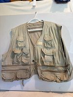 Front view of light khaki fly fishing vest hanging on hanger