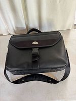 Front view of black Samsonite bag with flap, buckle, shoulder strap