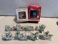 Boxed Norman Rockwell and M.I. Hummel ball ornaments with 8 Santa sleigh pendants displayed