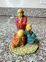Front view of three-monk ceramic figurine showing colors and posture