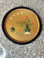 Full view of round plaque showing vase, flowers, censer, bird, characters, frame