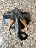 Front view of carved wood elephant head with tusks and curled trunk