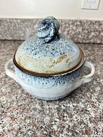 Side view of lidded stoneware casserole showing glaze, handles, and knob