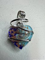 Front view of glass heart pendant showing aqua, cobalt and copper swirl under silver wire wrap