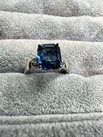 Front view of ring showcasing emerald-cut blue center stone and accent stones