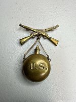 Front view of brass hat pin showing crossed rifles and canteen
