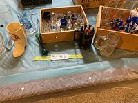 Overview showing assorted shot glasses, beer mugs, ceramic boot stein, black mug, clear stein, and box of stir sticks